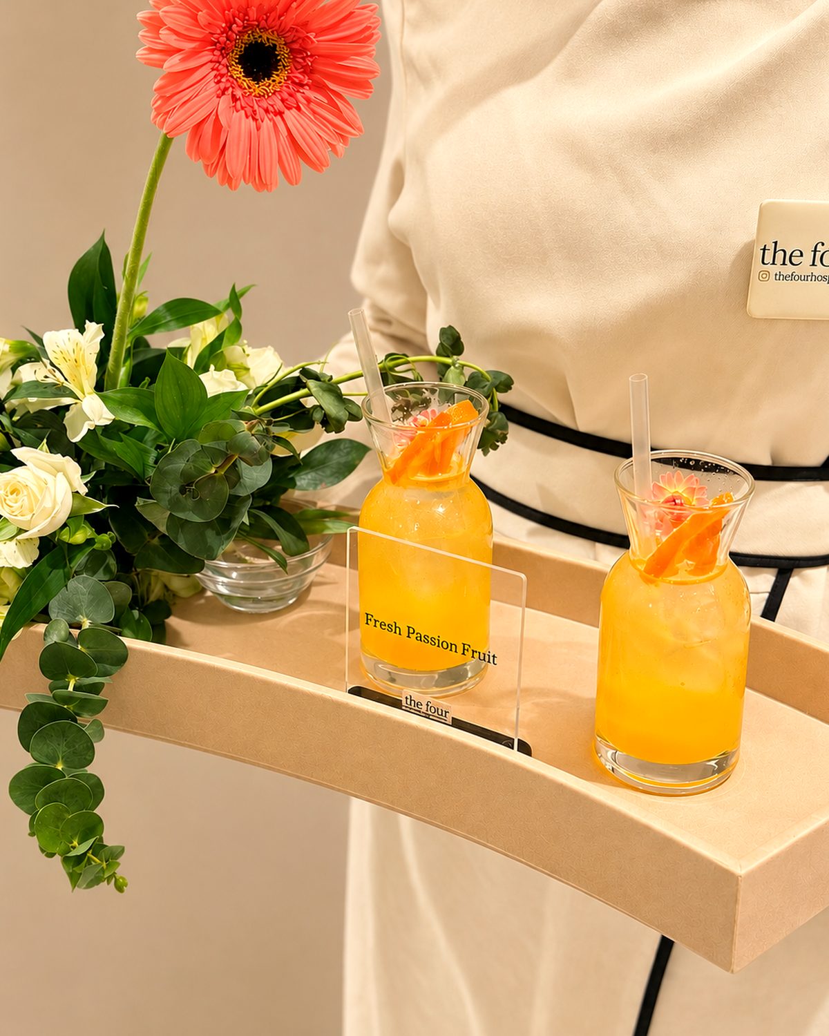 one of our sisters holding a styled tray with two fresh passion fruit drinks and flowers