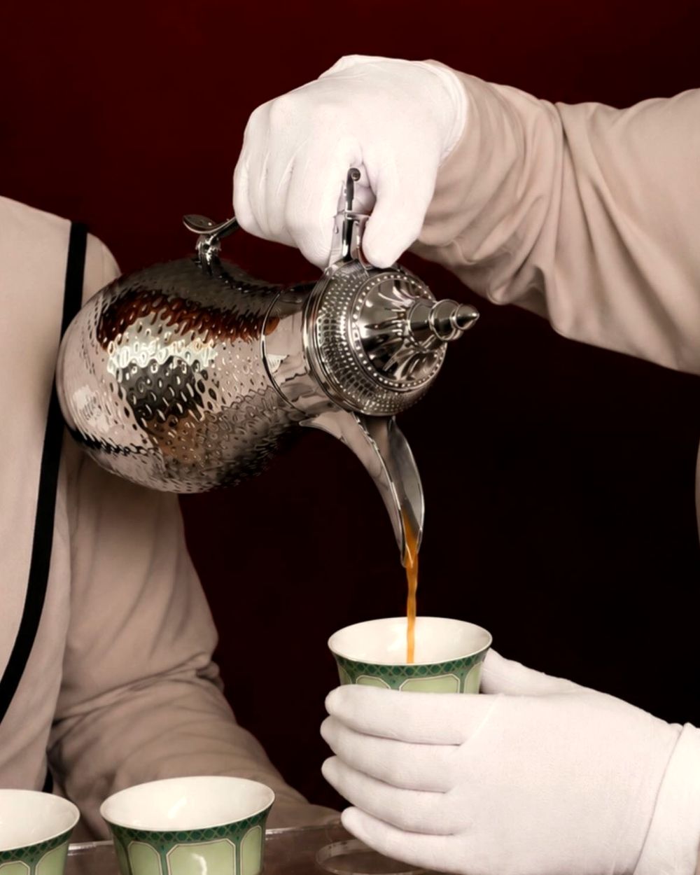 white-gloved hands pouring saudi coffee into small cups